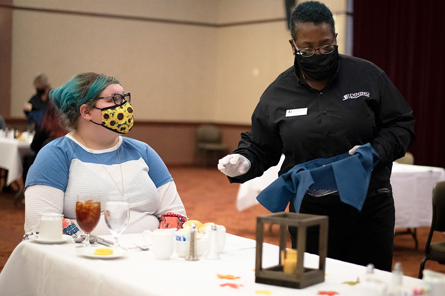A masked student and server at a dinner table