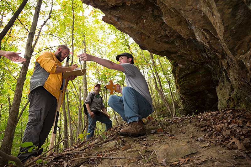 students by a cave examining rock samples