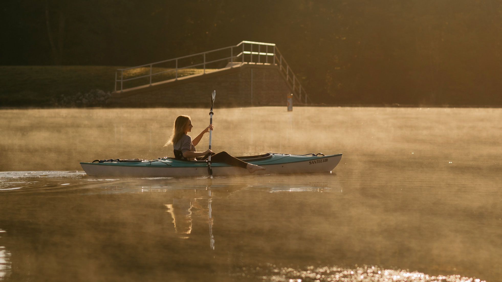 Person kayaking on a misty lake at sunrise