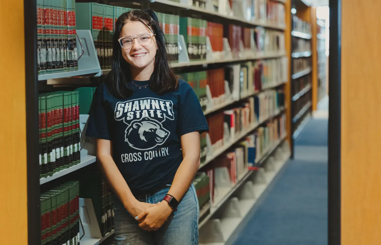 Student standing against bookshelf