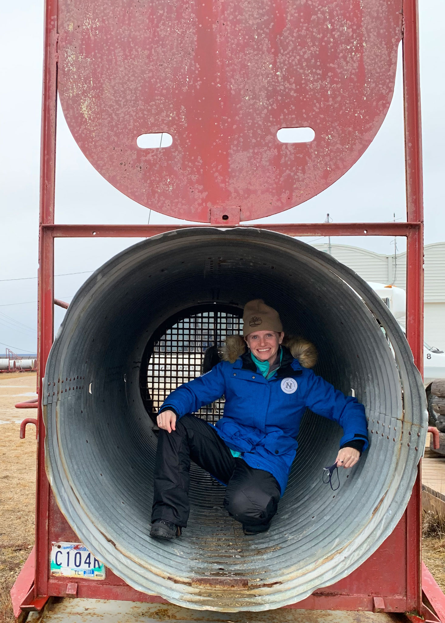 Person sitting inside a large metal culvert outdoors, smiling at the camera