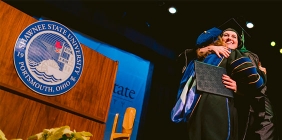 picture of student in cap and gown hugging someone on stage